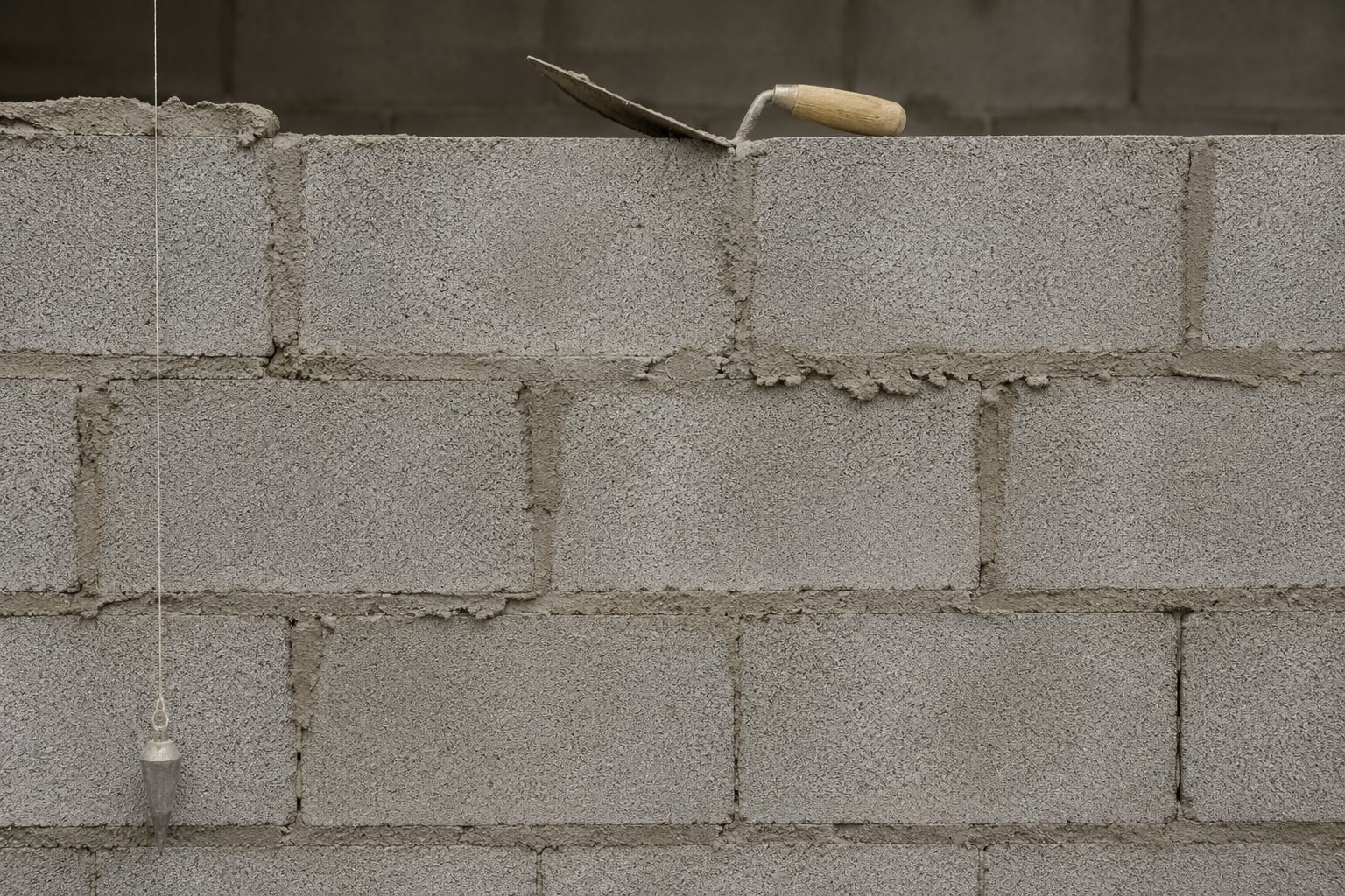 Mur de blocs béton en cours d'élévation, joints de mortier frais, truelle posée sur la dernière rangée